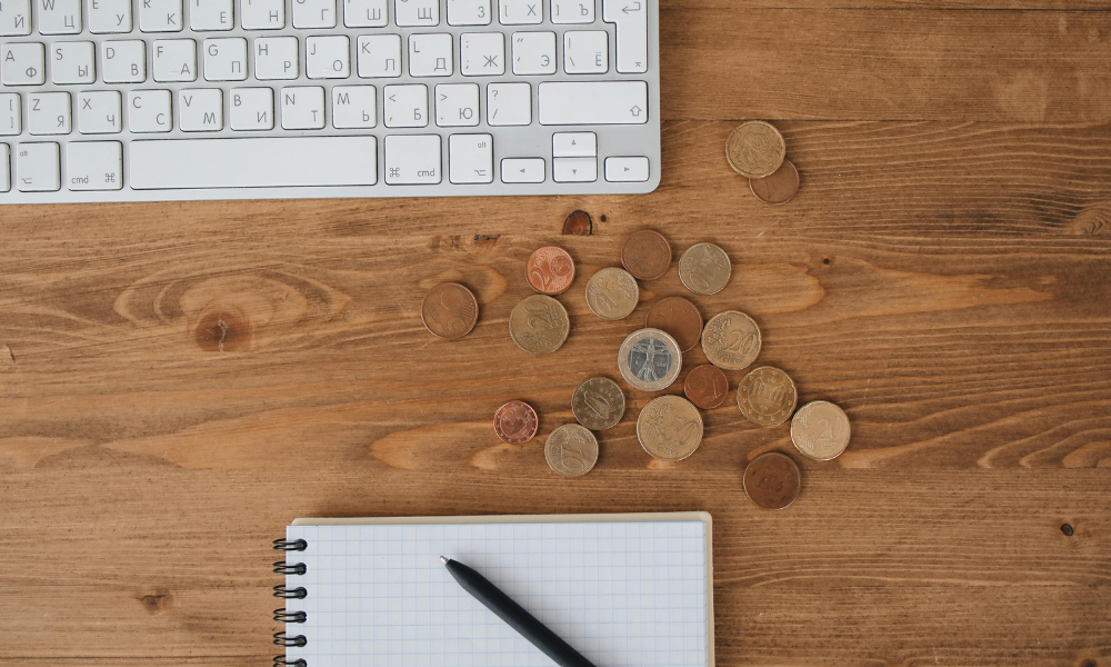 Monedas sobre una mesa junto a un cuaderno y un teclado, simbolizando la tesorería disponible y la gestión financiera necesaria para calcular el remanente de tesorería.