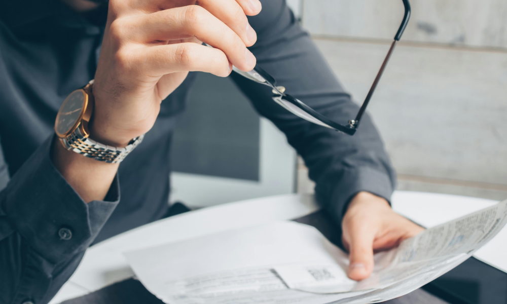 Persona revisando documentos financieros con un bolígrafo en la mano, representando el análisis de tesorería y la revisión de pagos y cobros en una empresa.