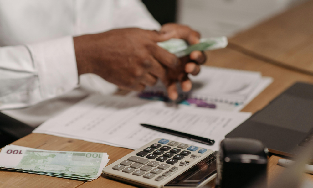 Persona contando billetes sobre una mesa con documentos, calculadora y material de oficina, representando la gestión de la tesorería y el control del dinero en una empresa.