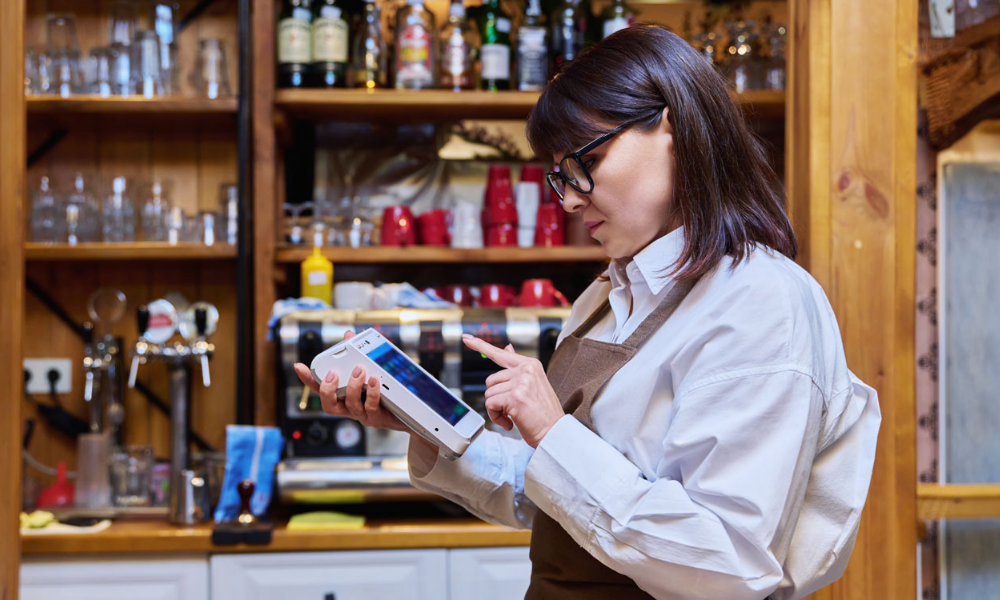 Camarera usando un terminal TPV en su negocio para gestionar cobros, representando el uso del TPV Sabadell en comercios y autónomos.