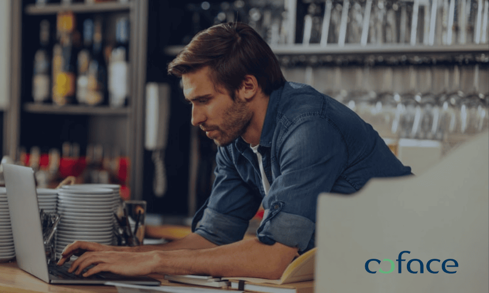 Emprendedor trabajando con su portátil en un establecimiento bajo la protección y servicios de Coface.