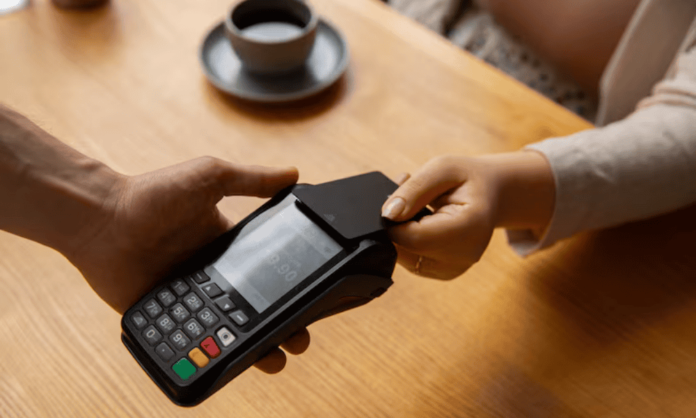 Cliente realizando un pago con tarjeta de crédito en un datáfono móvil inalámbrico en una cafetería.