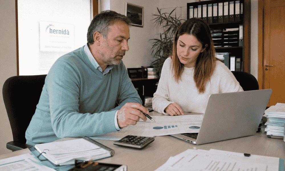 Responsable financiero elaborando un presupuesto empresarial junto a una compañera con informes económicos y ordenador.