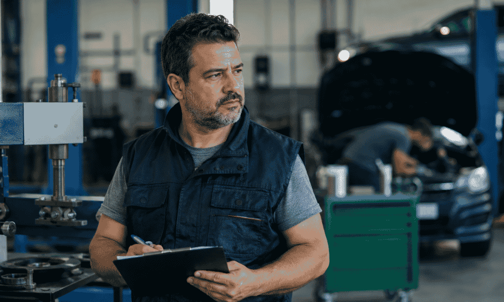 Jefe de taller supervisando el trabajo en un taller mecánico con una carpeta de control.