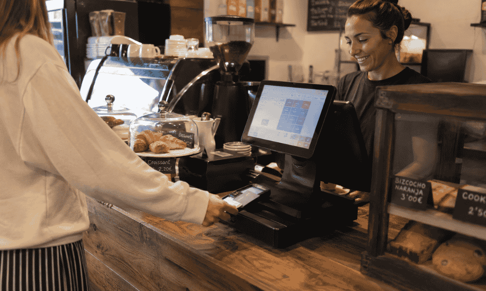Cliente pagando con tarjeta en la barra de una cafetería mediante un TPV para hostelería.