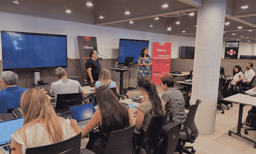 Formación para empresas en The Bridge con dos ponentes y participantes con ordenadores portátiles.