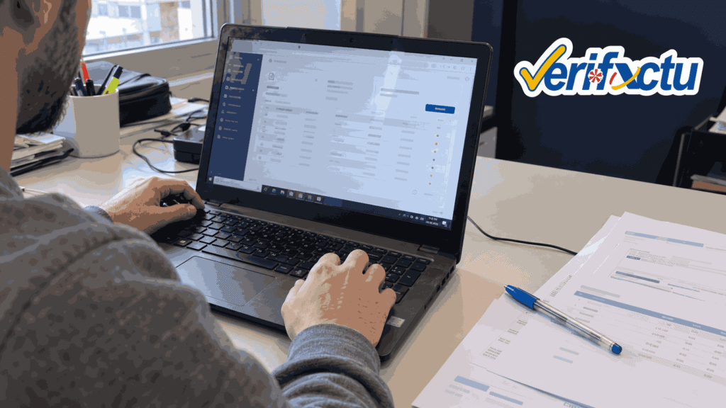 Profesional revisando facturas en un portátil de oficina con el logotipo de VeriFactu.