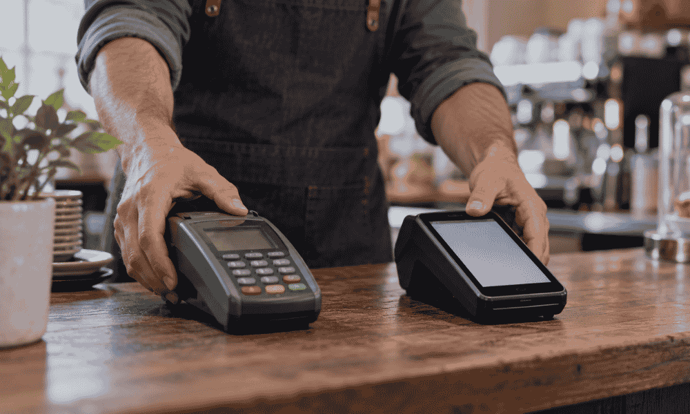 Comerciante sustituyendo un TPV antiguo por un datáfono nuevo en el mostrador de su negocio.