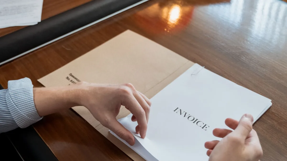 Persona sujetando una factura proforma impresa sobre una mesa de oficina de madera
