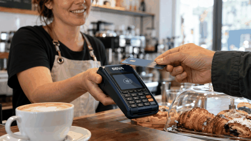 Autónoma de una cafetería cobrando a un cliente con tarjeta mediante un datáfono BBVA.